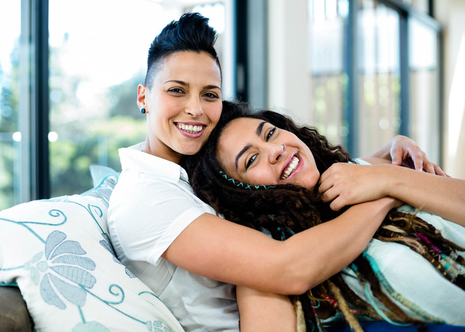Smiling lesbian couple embracing and relaxing on sofa